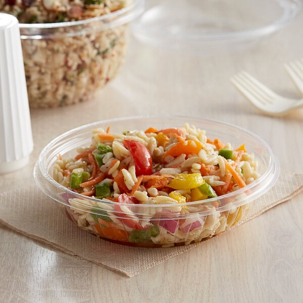 A Dart clear plastic bowl filled with food on a table.