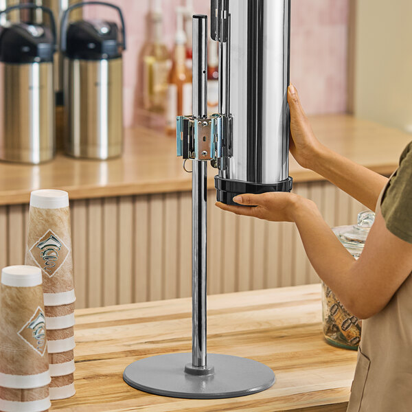 A woman using a silver Modular Countertop Cup Dispenser on a counter.