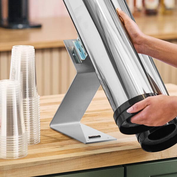 A person using a Modular Countertop Stainless Steel Cup Dispenser on a counter.