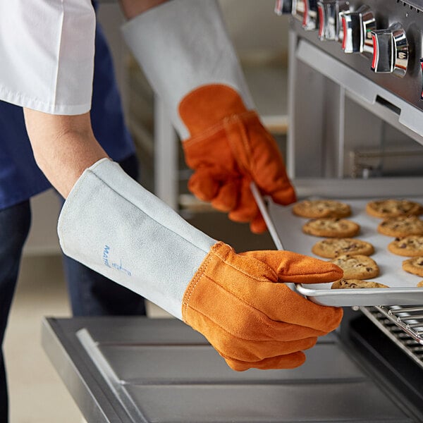 A person wearing Matfer Bourgeat leather oven gloves holding a tray of cookies.