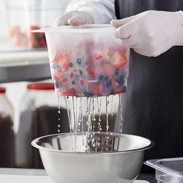 A gloved hand uses a Cambro 1/6 size colander to rinse strawberries in a plastic container.