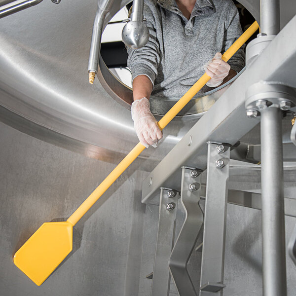 A person using a yellow Carlisle Sparta paddle with a yellow pole to clean a metal pipe.