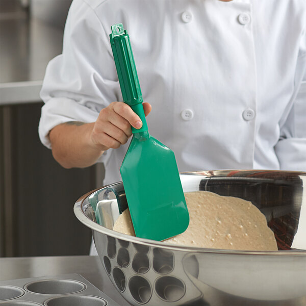 A woman in a white chef's coat using a Carlisle green paddle to mix dough in a bowl.