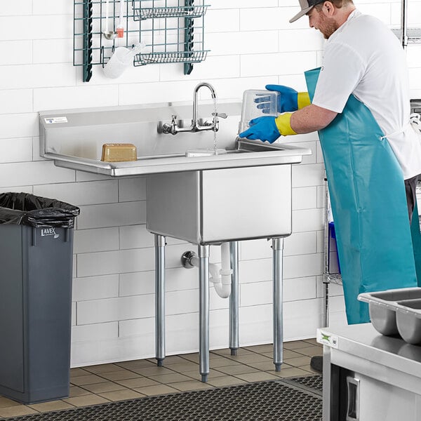 A man wearing a blue apron and gloves washing a Steelton commercial sink over a counter.