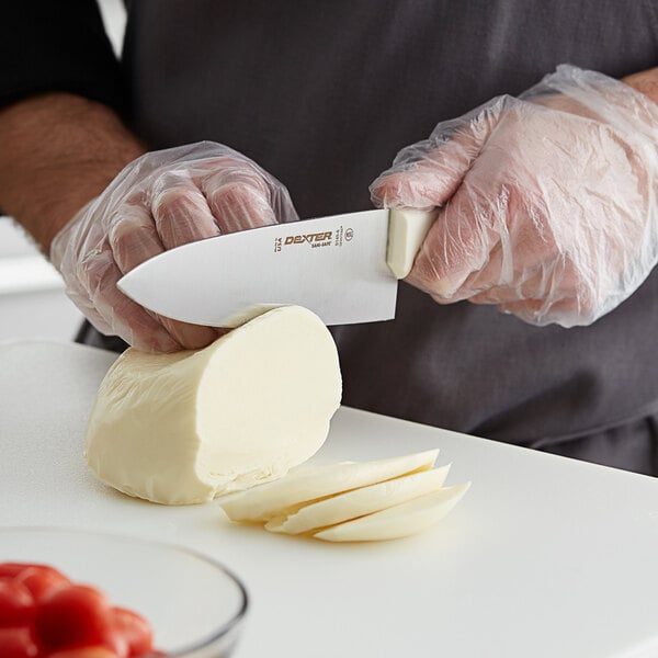 A person cutting a piece of cheese with a Dexter-Russell 6" Chef Knife.