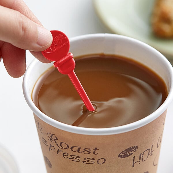 A hand holding a Royal Paper red beverage stirrer in a cup of coffee.