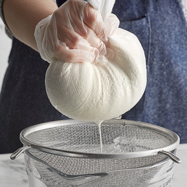 A person in gloves holding a white ball of cheese wrapped in San Jamar Grade 10 bleached cheesecloth.