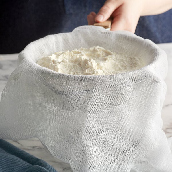 A person using San Jamar Grade 10 bleached cheesecloth to strain white food.
