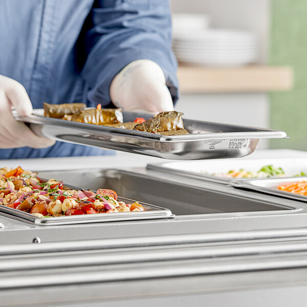 A person in a white coat holding a Vollrath stainless steel steam table tray of food.