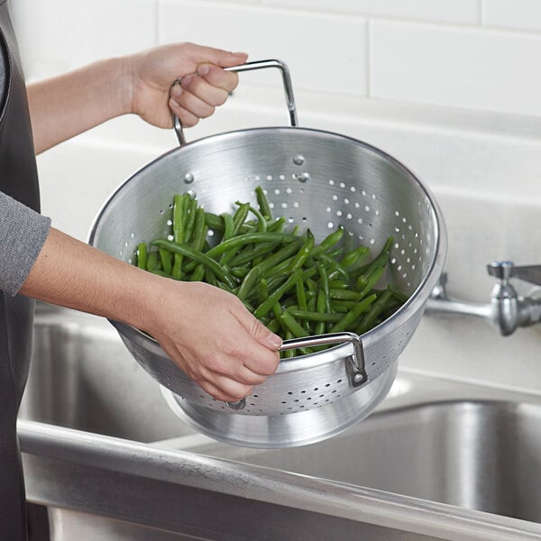 a hand holding a colander full of green beans