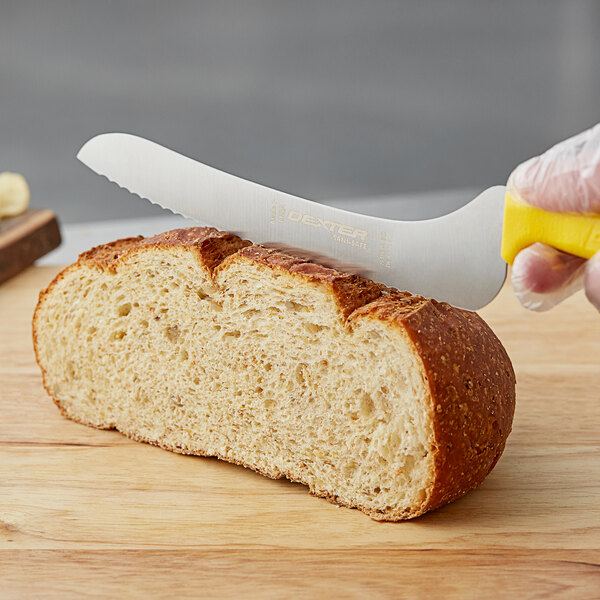 A person using a Dexter-Russell yellow scalloped bread knife to cut a loaf of bread.