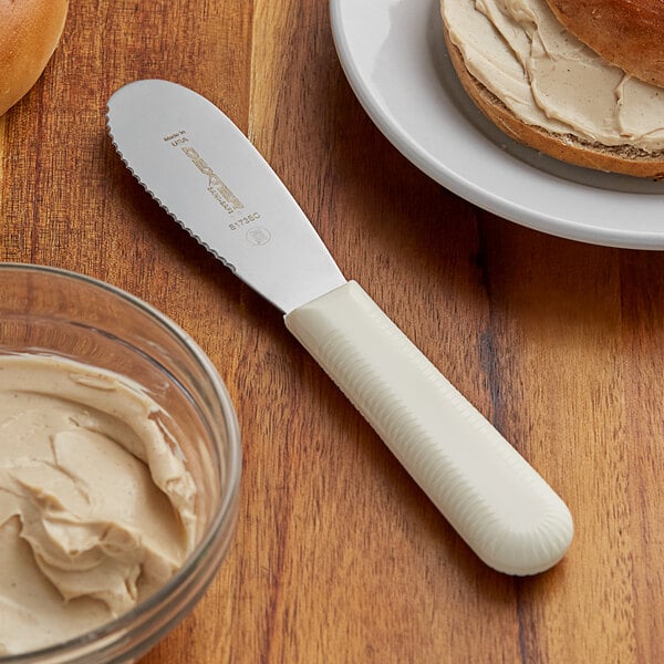 A Dexter-Russell scalloped sandwich spreader next to a bowl of butter on a table.