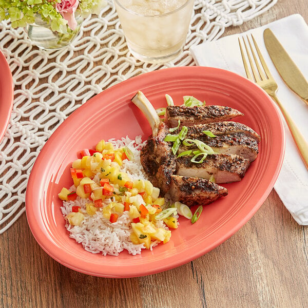 An Acopa Capri coral reef oval stoneware platter with meat and rice, fruit salsa, and a flower.