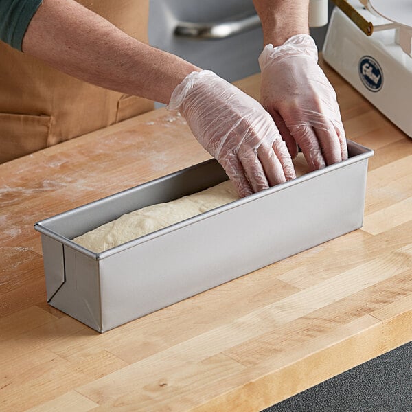 A person wearing gloves putting dough into a Baker's Mark aluminized steel loaf pan.