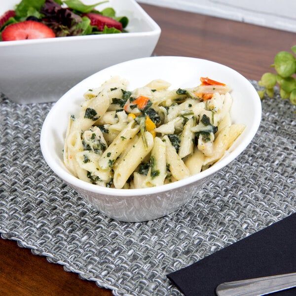 A white porcelain pinch bowl filled with pasta and vegetables.