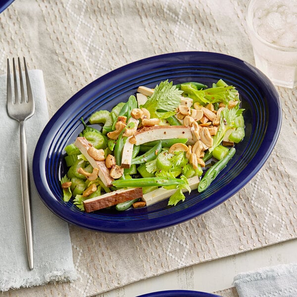 An Acopa Capri deep sea cobalt oval stoneware platter with a salad on it.