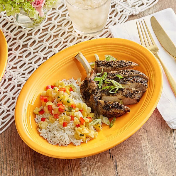 An Acopa mango orange oval stoneware coupe platter with food on a table.