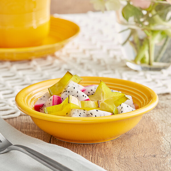 A yellow Acopa Capri stoneware fruit bowl on a table with fruit in it.