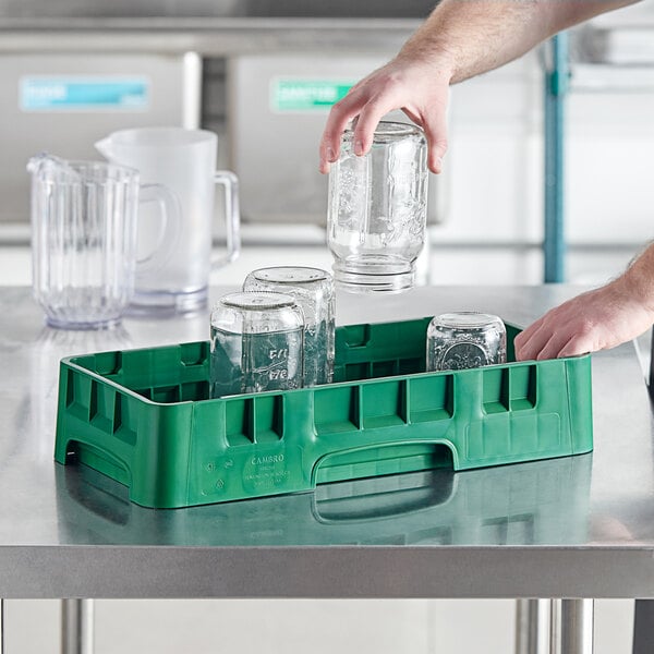 A person putting glasses into a green Cambro dish rack.