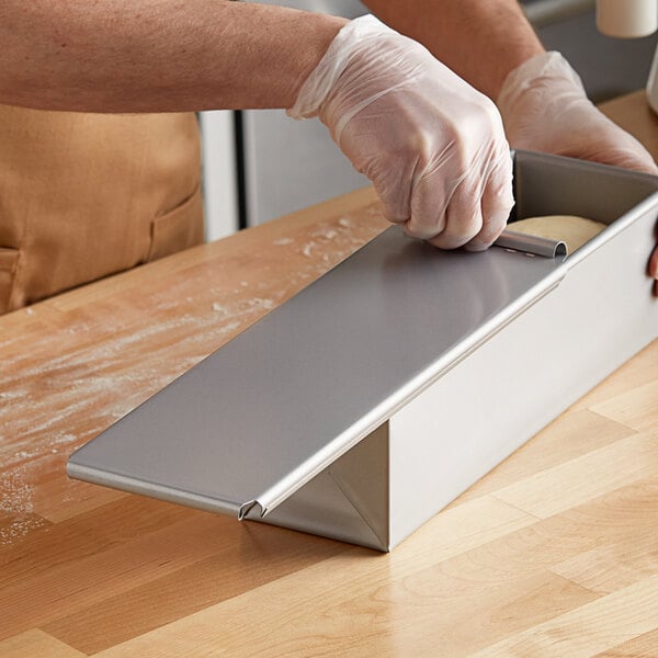 A person wearing gloves slides a metal cover onto a Baker's Mark Pullman bread pan.