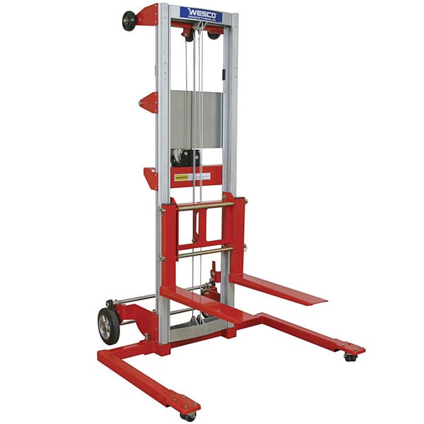 A red and silver Wesco hand winch lift with adjustable straddle forks.