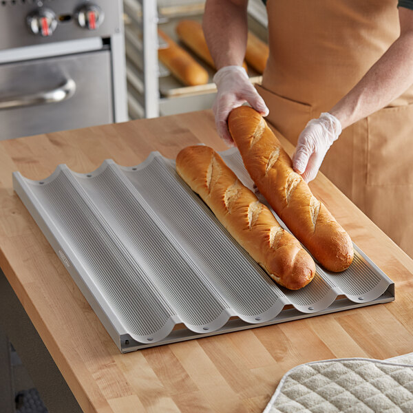 A person holding two long loaves of bread on a Baker's Lane baguette pan.