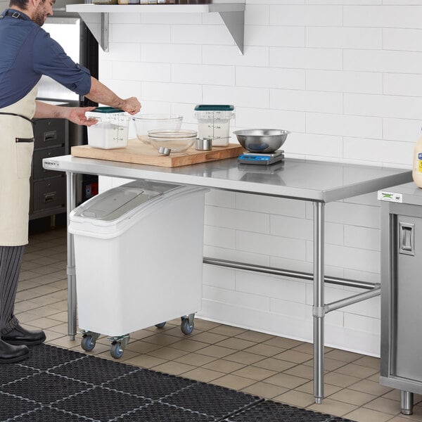 A man in an apron standing next to a Regency stainless steel open base work table.