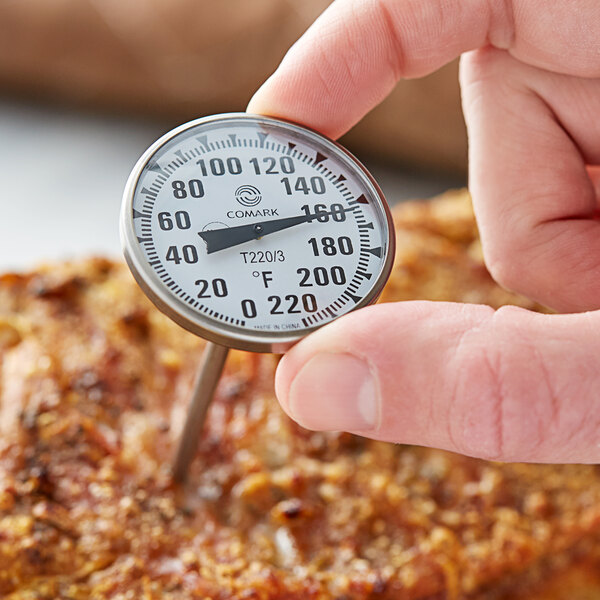 A person using a Comark pocket probe thermometer to check the temperature of meat.