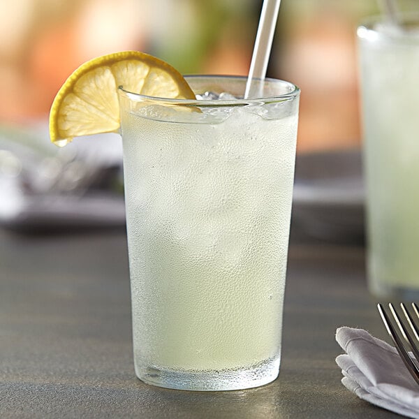 A Duralex glass of lemonade with a straw in it, sitting on a table.