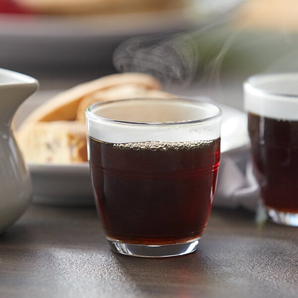 A Duralex glass of brown liquid on a table.