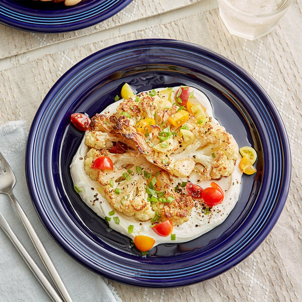 A plate of food with vegetables and a fork on a blue Acopa Capri stoneware plate.