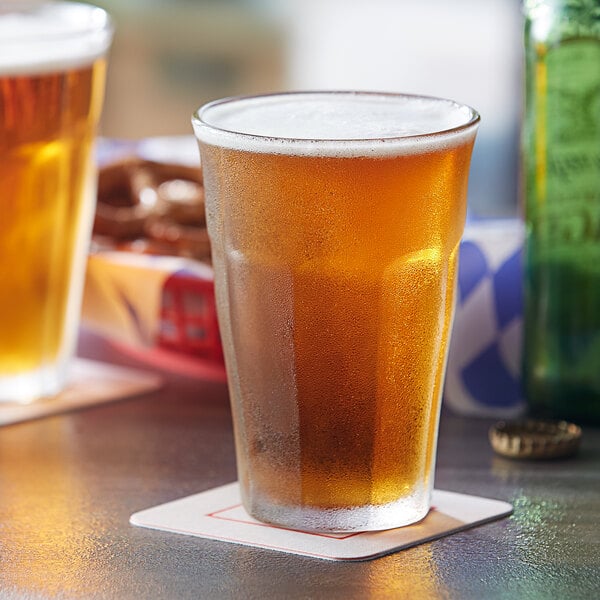 Two Duralex Picardie highball glasses of beer on a table next to a plate of pretzels.