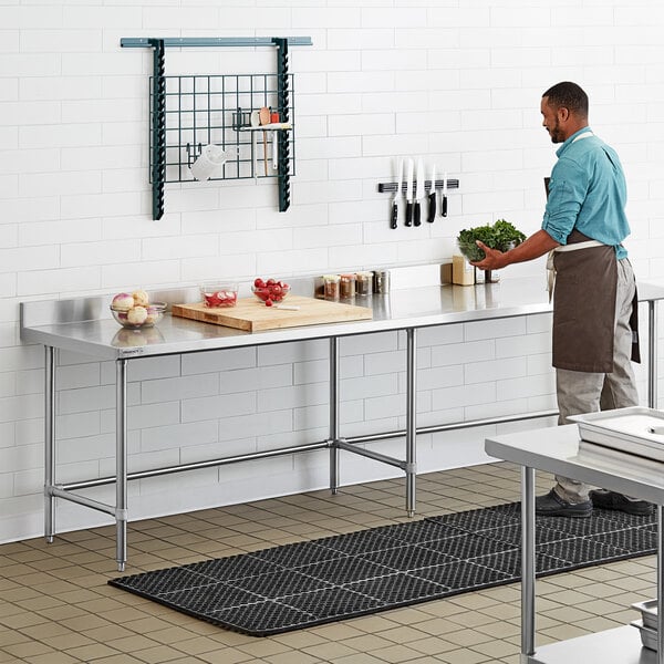 A man standing at a Regency stainless steel work table in a professional kitchen.