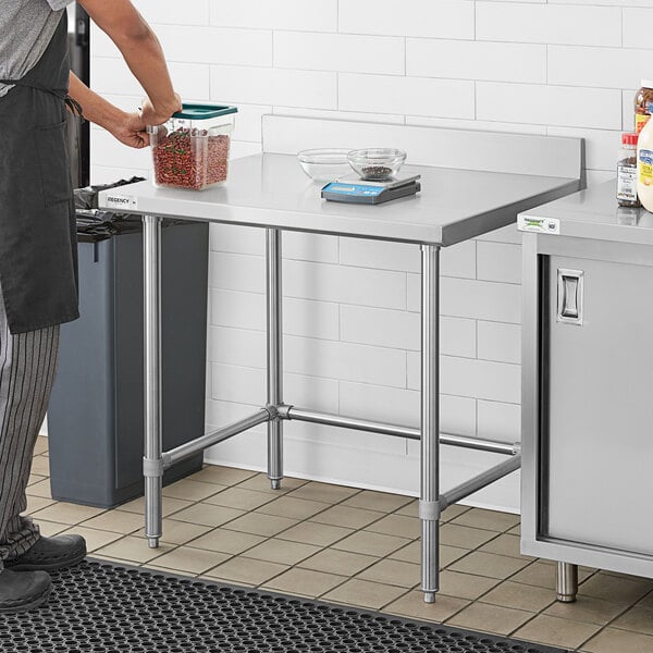 A man in an apron standing next to a Regency stainless steel open base work table.