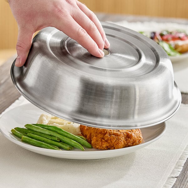 A hand using an American Metalcraft stainless steel plate cover over a plate of food.