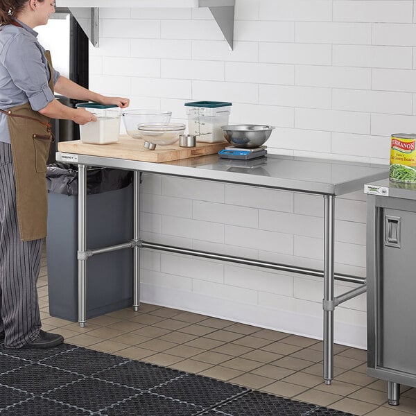 A woman wearing an apron standing at a Regency stainless steel open base work table.