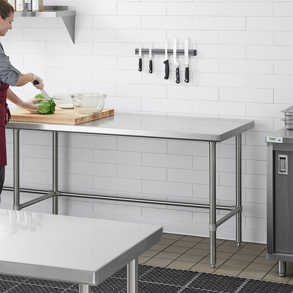 A woman in a kitchen preparing food on a Regency stainless steel work table.