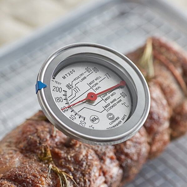 A Comark 4 1/2" probe dial meat thermometer gauge on a piece of meat.
