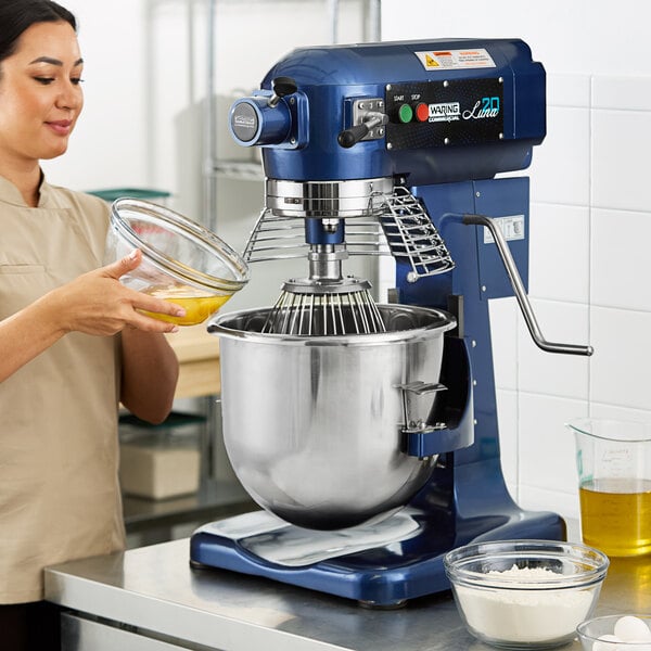 A woman using a Waring Planetary Stand Mixer with a glass bowl to mix white powder.