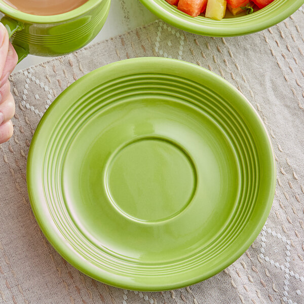 A green Acopa Capri stoneware saucer on a table with a cup of coffee.