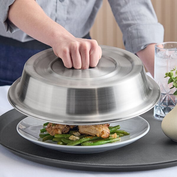 A stainless steel satin finish plate cover being lifted from a plate of food.