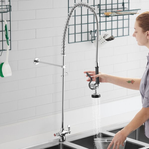 A woman using a deck mount pre-rinse faucet to wash dishes in a professional kitchen.