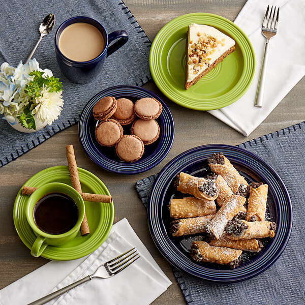 A table with green Acopa Capri stoneware cups filled with brown liquid and a plate of food with a piece of cake.