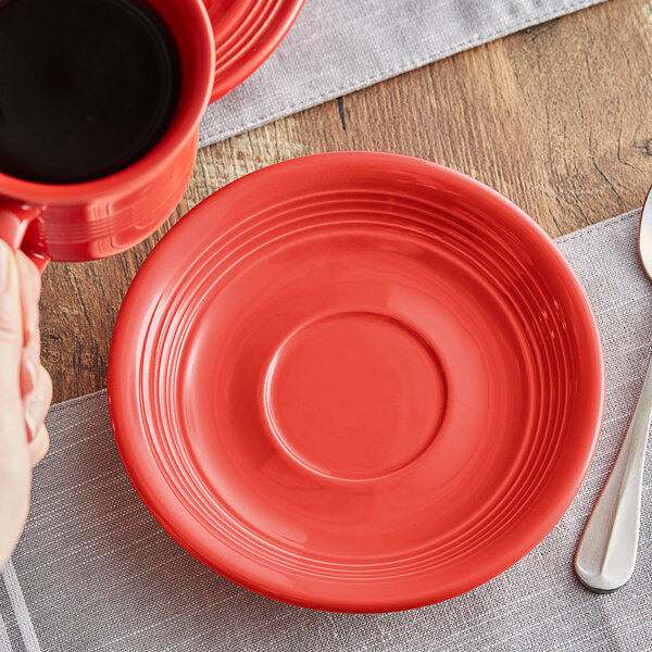 A person holding a red Acopa Capri saucer with a spoon and a fork.