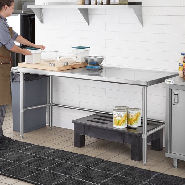 A woman in a professional kitchen standing in front of a Regency stainless steel work table.