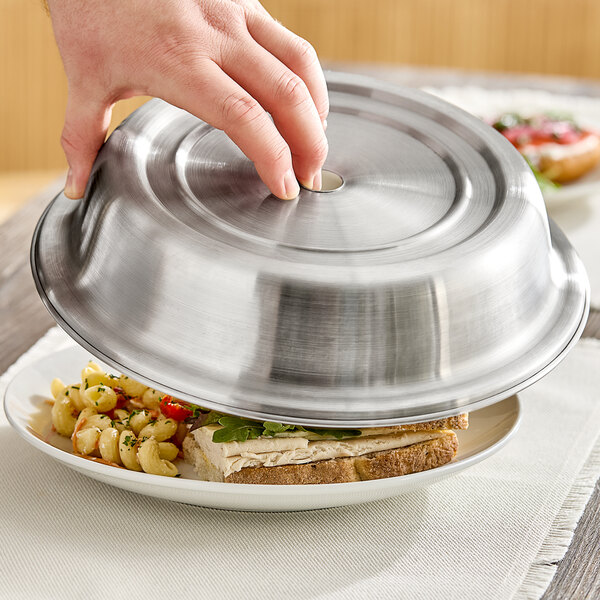 A hand using an American Metalcraft stainless steel plate cover to place over a plate of food.
