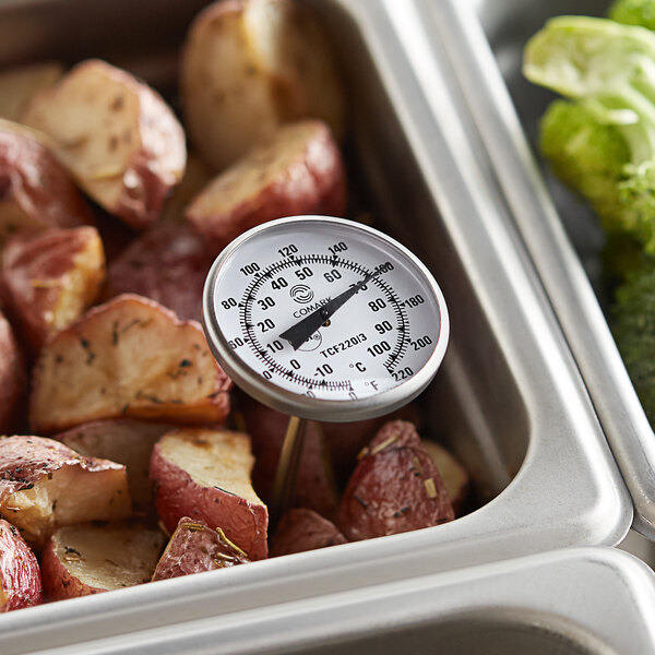 A Comark pocket probe thermometer in a metal container of potatoes on a counter.