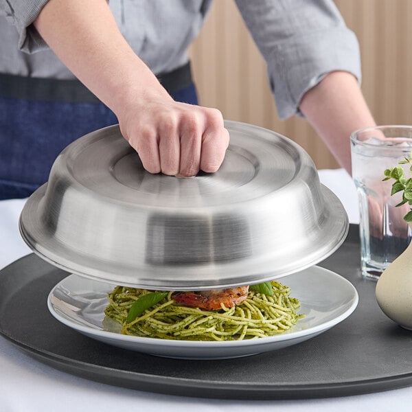 A stainless steel satin finish plate cover being lifted off a plate of food.