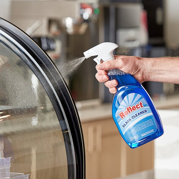 A hand using Noble Chemical Reflect Ready-to-Use Glass Cleaner to spray a glass door.