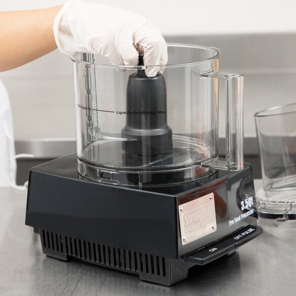 A person wearing gloves using a Waring S blade in a black container.